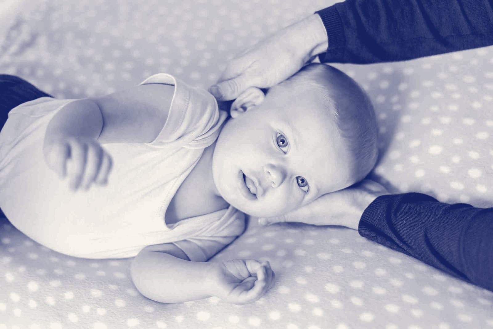 A baby lying on a spotted blanket while an osteopath gently holds their head