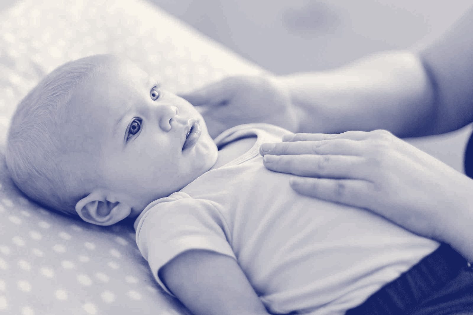 An osteopath's hands resting gently on a baby's tummy