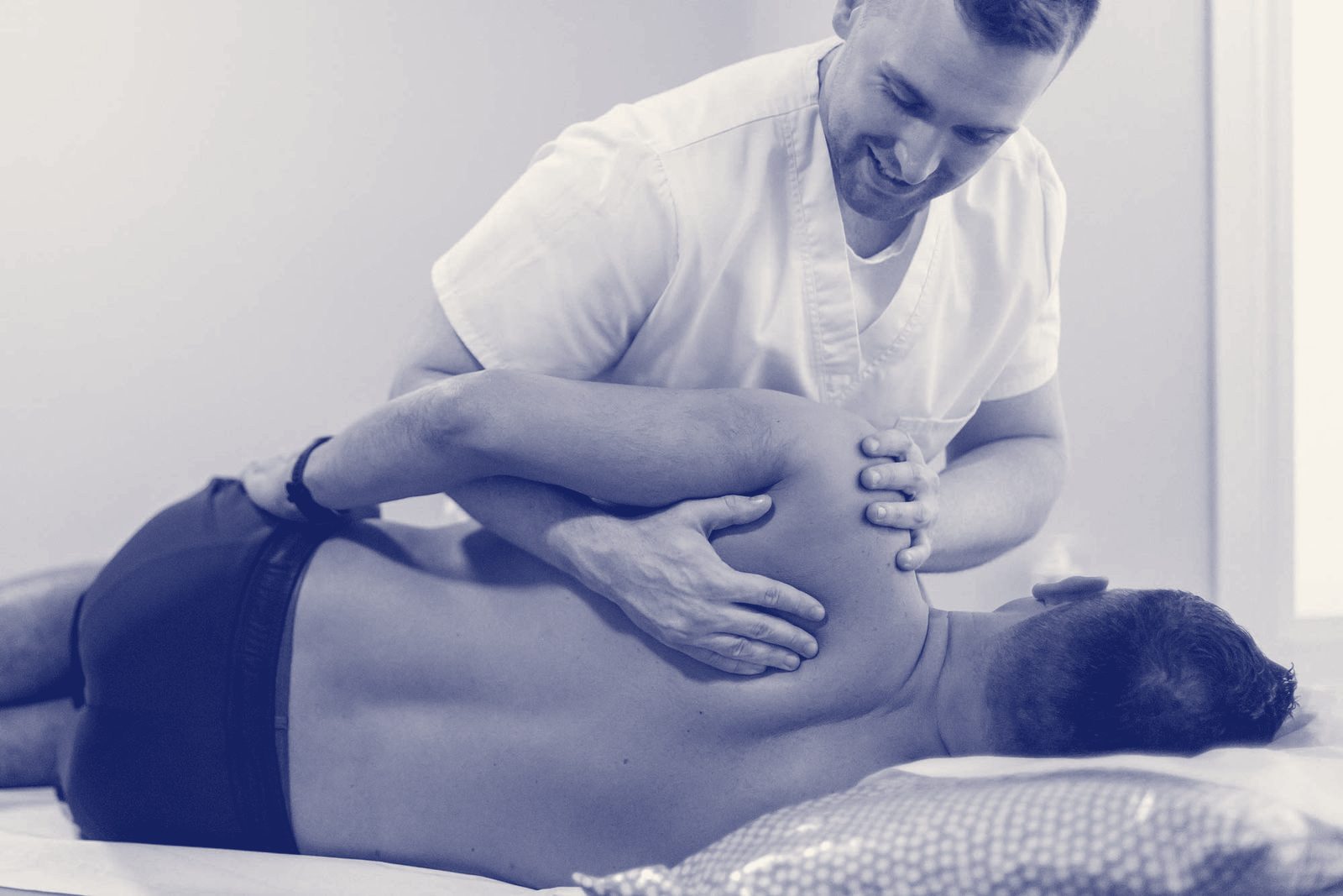 An osteopath stretching a patient's back and shoulder on a treatment couch