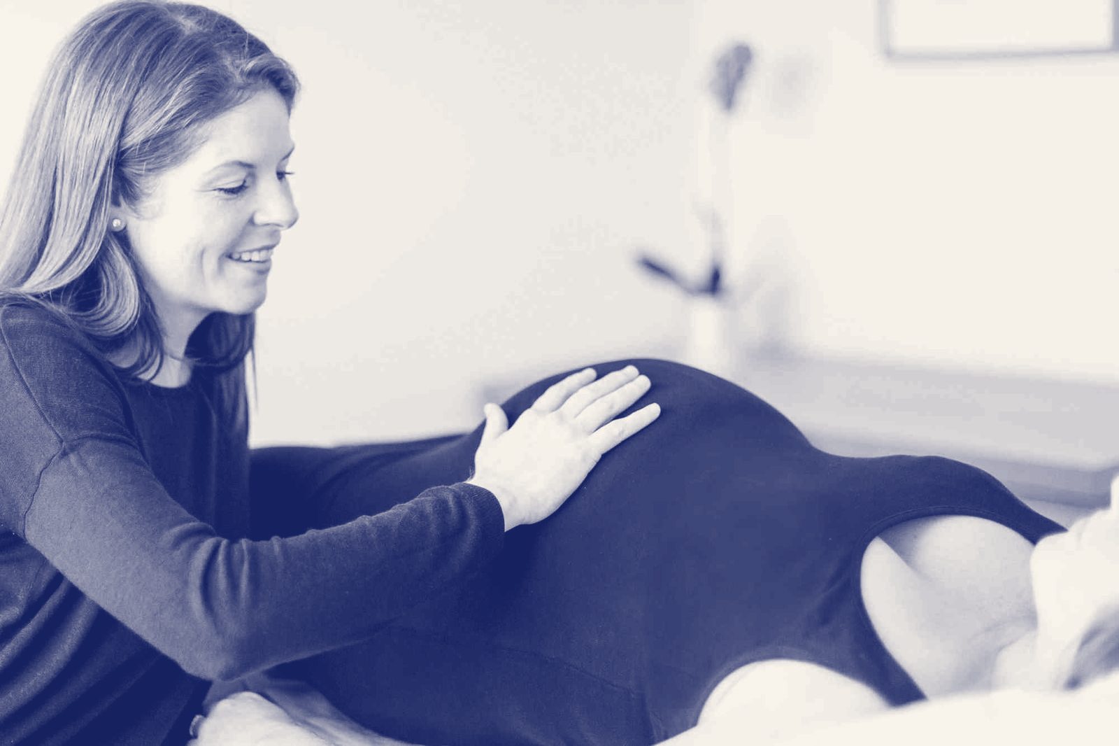 An osteopath gently treating a pregnant patient lying on her side