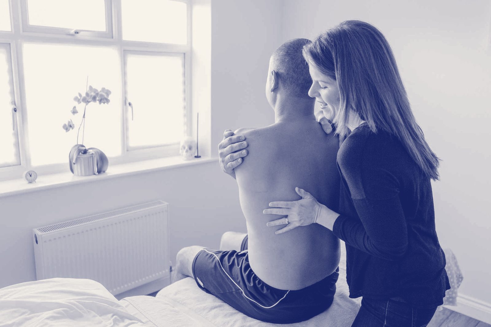 An osteopath examining an older man's shoulder by a sunny window